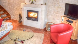 Un salon confortable avec une cheminée, un téléviseur et un fauteuil rouge.