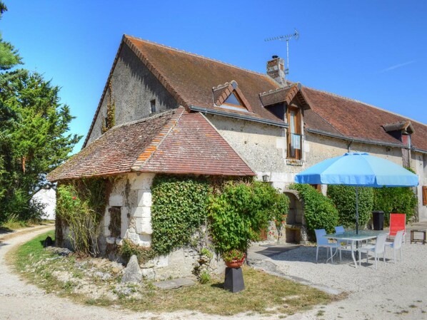 A rustic stone building with a tiled roof, a gravel driveway, and a patio area with outdoor seating.