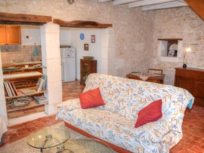 A cozy living room with a sofa, a glass coffee table, and a kitchen area with a refrigerator and cabinets.