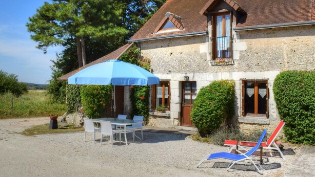 Une maison en pierre avec un toit en tuiles, un espace extérieur couvert avec une table et des chaises, et une allée gravillonnée.
