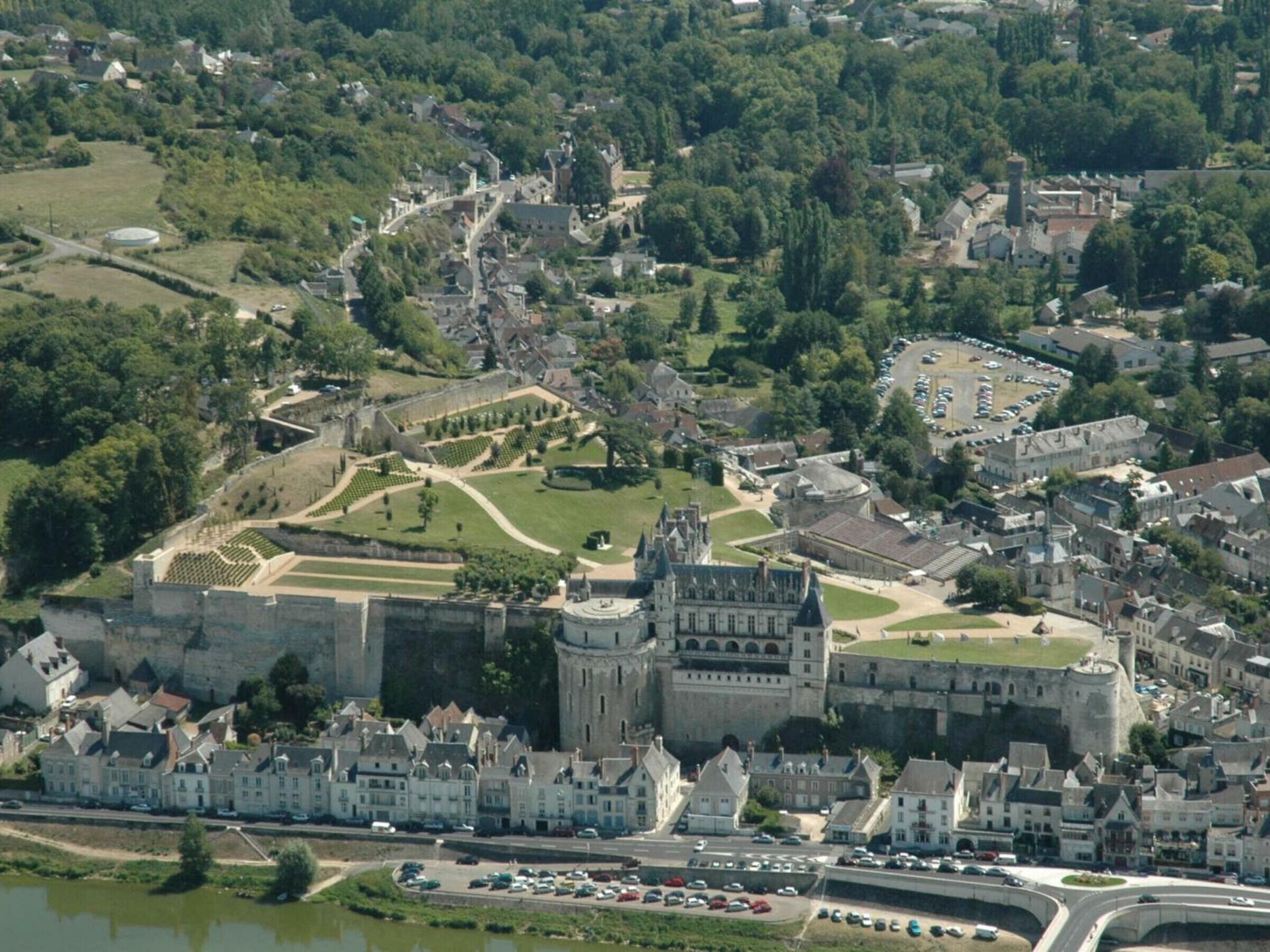 Une vue aérienne d’une ville historique, avec un château imposant, entourée de bâtiments résidentiels et traversée par une rivière.
