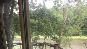 A wooden deck with a metal railing, overlooking a body of water and trees.