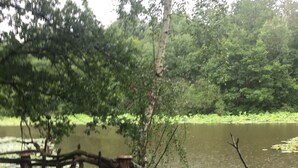 A wooden deck with a chair and a small table, overlooking a calm body of water with trees in the background.