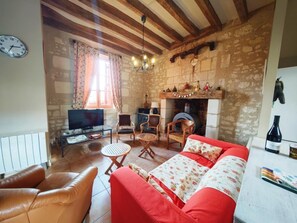 A cozy living room with a stone fireplace, leather sofa, wooden chairs, and a television.