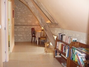 A room with a sloped ceiling, a wooden bookshelf filled with books, a wooden chair, and a small table.
