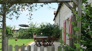 A wooden gate leading to a patio with a table and chairs, surrounded by greenery and a building with red shutters. - Touraine Cottage near Loches with Fireplace and Garden (Saint-Senoch)