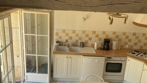 Une cuisine compacte avec des meubles blancs, un lave-vaisselle, un four, une machine à café et un dosseret à carreaux.