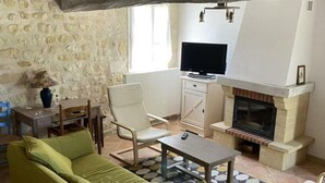 Un salon avec un mur en pierre, une cheminée, un téléviseur et un canapé vert.
