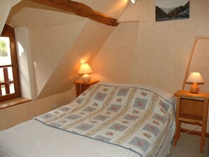 Um quarto de sótão aconchegante com teto inclinado, uma cama com colcha floral, duas luminárias de cabeceira e uma janela com vista para montanhas.