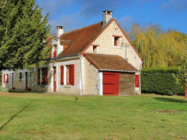 Une ferme en pierre avec un toit recouvert de tuiles rouges, une porte en bois et un petit abri attenant.