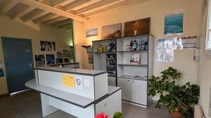 Een receptiebalie met een plant, een poster en een deur in een ruimte met betegelde vloer en houten plafond.