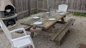 Een houten picknicktafel met bankjes, een barbecue en een witte stoel.