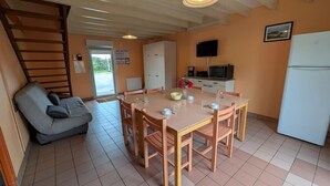 Een kleine keuken met een eettafel, stoelen, een bank, een koelkast, een magnetron en een televisie.