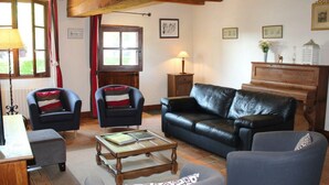 A cozy living room with a leather sofa, two armchairs, a wooden coffee table, and a piano. - Charming 18th Century Cottage with Pool, Near Loire Castles and Vineyards (Saint-Épain)