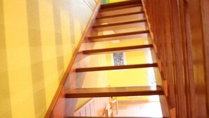 A wooden staircase with a handrail, leading to a room with a yellow wall and a window. - Semi-Detached Home in Omonville-la-Rogue with Parking and Pets Allowed (Omonville-la-Rogue)