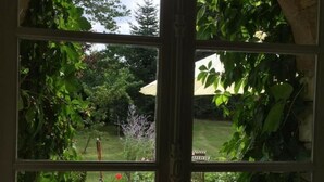 A view through a window with a garden, a wooden deck, and a patio area. - Charming cottage in Chinon forest with private garden (Saint-Benoît-la-Forêt)