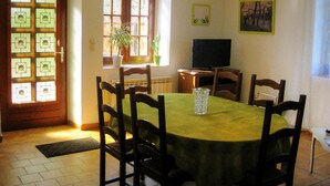 Zona pranzo con un tavolo rotondo, sedie, una televisione e una finestra con piante.