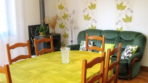 Zona pranzo con un tavolo verde, sedie in legno e un divano verde con cuscini decorati.