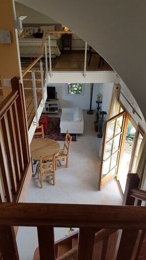Un espacio habitable de varios niveles con una escalera, una zona de comedor con mesa y sillas, un sofá y un gran ventanal que proporciona luz natural.