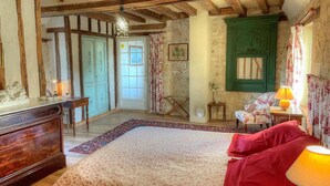 A traditional room with exposed wooden beams, a bed with floral bedding, a green door, and a small table with a lamp. - Charming 17th-Century Farmhouse with Garden, Terrace, Modern Amenities, and Wi-Fi in Villandry (Villandry)