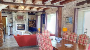 A rustic dining area with a wooden table and plaid chairs, a fireplace, and stone walls. - Charming 17th-Century Farmhouse with Garden, Terrace, Modern Amenities, and Wi-Fi in Villandry (Villandry)