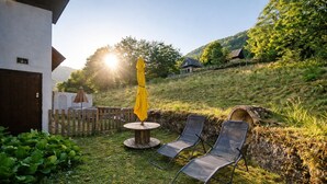 Un jardín con valla de madera, una mesa con sombrilla amarilla y dos sillones de descanso.