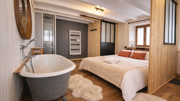 Un dormitorio moderno con una bañera grande, una cama con edredón blanco y suelo de madera.