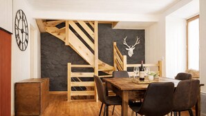 Un comedor con una mesa de madera, sillas, una botella de vino y un adorno de cabeza de ciervo en la pared.