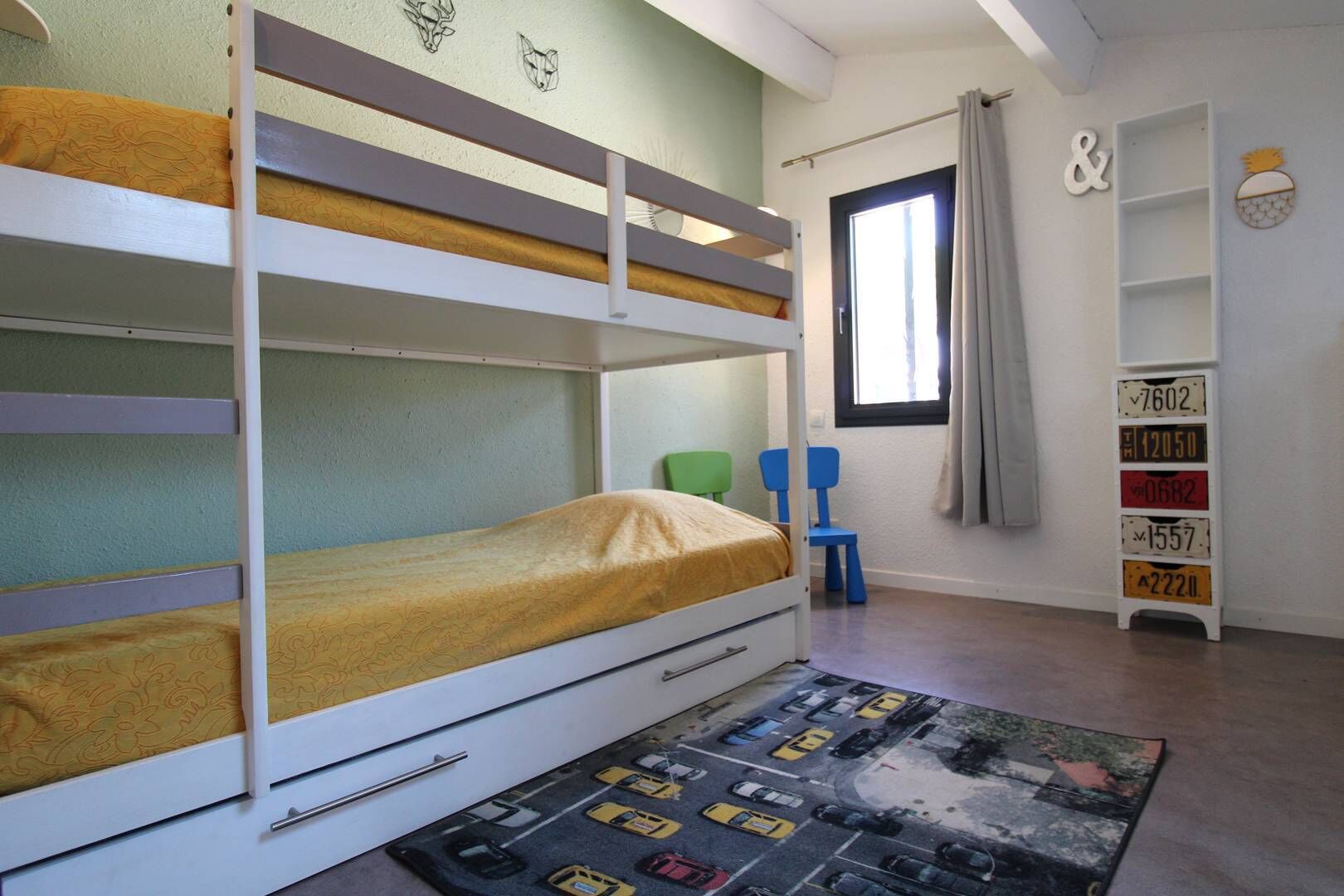 A bunk bed with a yellow mattress, a green chair, and a car-themed rug.