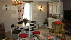 Ein Essbereich mit einem runden Tisch, Stühlen, einer Chandelüster und einem Fenster mit floralen Vorhängen.