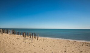 Una playa arenosa con una valla de madera y aguas azules tranquilas.