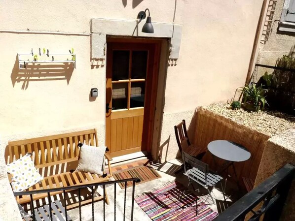 Un pequeño patio al aire libre con un banco de madera, una mesa y sillas.