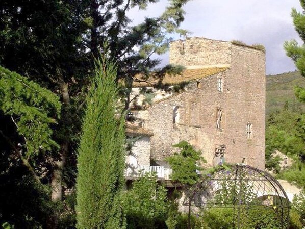 A historic stone building with a tower, surrounded by trees and greenery.
