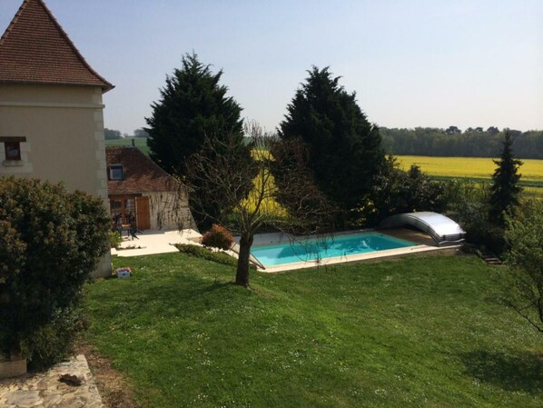 A residential property with a swimming pool, a detached house, and a large field in the background.