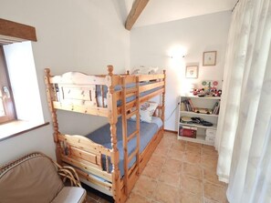 A bunk bed room with a wooden headboard, a bookshelf with toys, and a window with curtains.