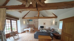 A spacious living area with a high ceiling, wooden beams, a dining table with chairs, a sofa, and a television. - Charming 17th-century home in Touraine with private pool (Abilly)