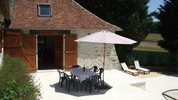 A rustic house with a tiled roof, a stone wall, and a patio with a table and chairs. - Charming 17th-century home in Touraine with private pool (Abilly)