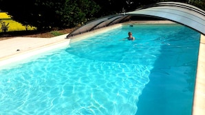 A swimming pool with clear blue water, surrounded by a tiled deck and a curved roof structure. - Charming 17th-century home in Touraine with private pool (Abilly)