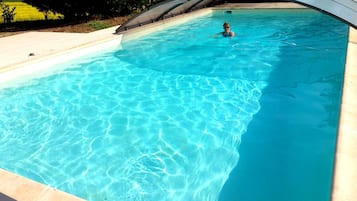 Een zwembad met helderblauw water, omgeven door een betegeld terras en een gebogen dakconstructie.