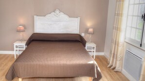 A bedroom with a large bed, two bedside tables with lamps, a window with curtains, and a radiator.