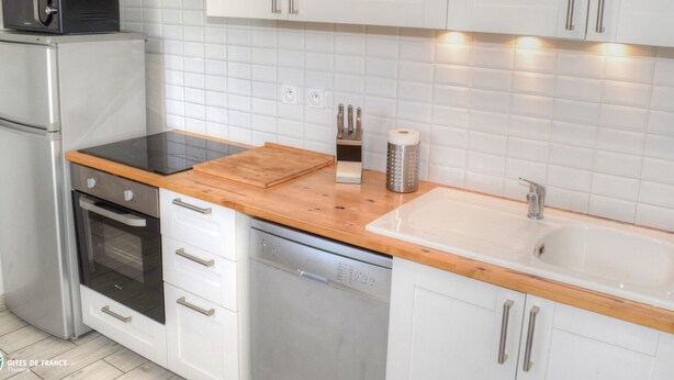 A modern kitchen with white cabinets, a wooden countertop, a built-in oven, a dishwasher, and a sink.