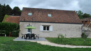 A single-story house with a tiled roof, a small porch with a table and chairs, and a green umbrella.