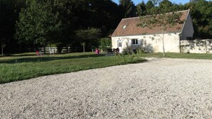A single-story building with a sloped roof, a gravel driveway, and a fenced area with trees.