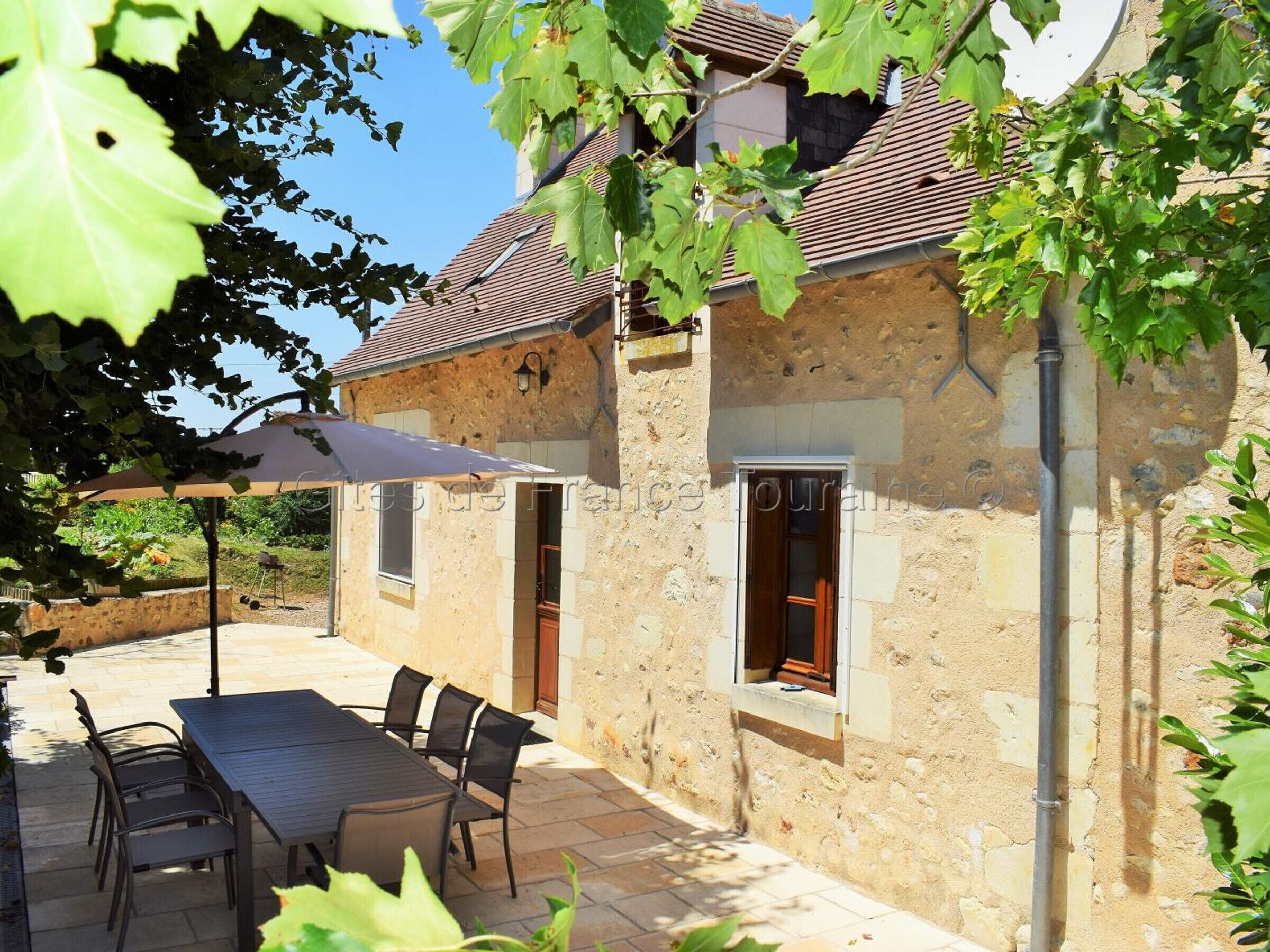 Ein Steinhaus mit Ziegeldach, Außenbestuhlung und einer Pergola.