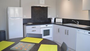 Uma cozinha moderna com eletrodomésticos brancos, bancada preta e mesa redonda com jogos americanos amarelos.