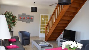 Uma sala de estar com escada, sofá, mesa de centro e televisão.