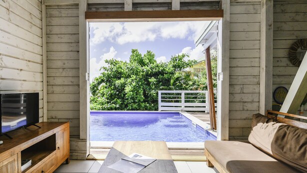 A room with a wooden ceiling, a TV on a wooden cabinet, a pool outside, and a sofa inside.