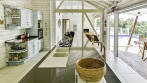 A modern kitchen with white cabinets, a long countertop, and a large window overlooking a pool.