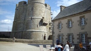 A historic stone tower with a circular top, adjacent to a building with multiple windows and a tiled roof. - Charming family apartment in central Saint-Vaast-la-Hougue with wifi (Saint-Vaast-la-Hougue)