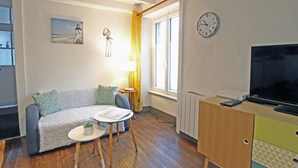 A cozy living room with a sofa, a small table with a lamp, a TV, and a clock on the wall. - Charming family apartment in central Saint-Vaast-la-Hougue with wifi (Saint-Vaast-la-Hougue)